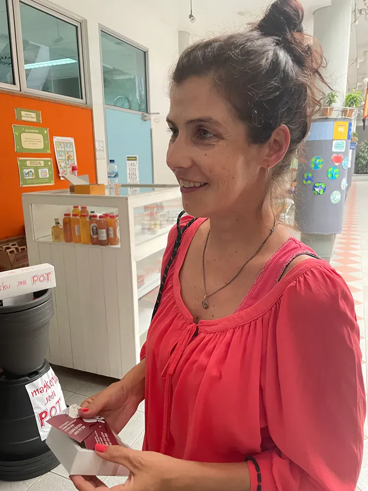 A woman in a pink shirt is holding a box and smiling.
