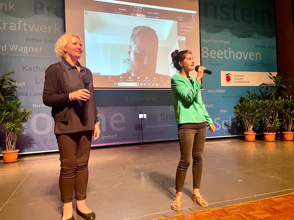 Two women singing on a stage in front of a screen that says beethoven