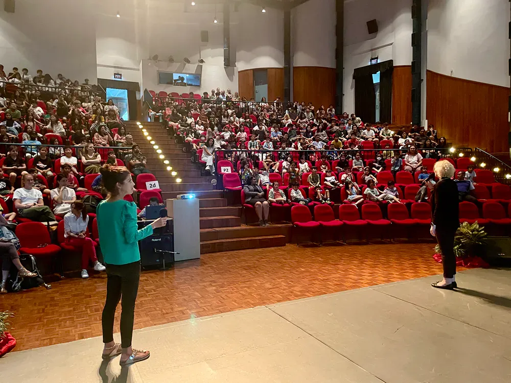 A woman is standing on a stage in front of an auditorium full of people.