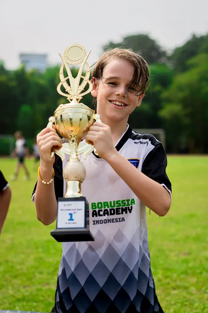 A young boy is holding a trophy on a field.