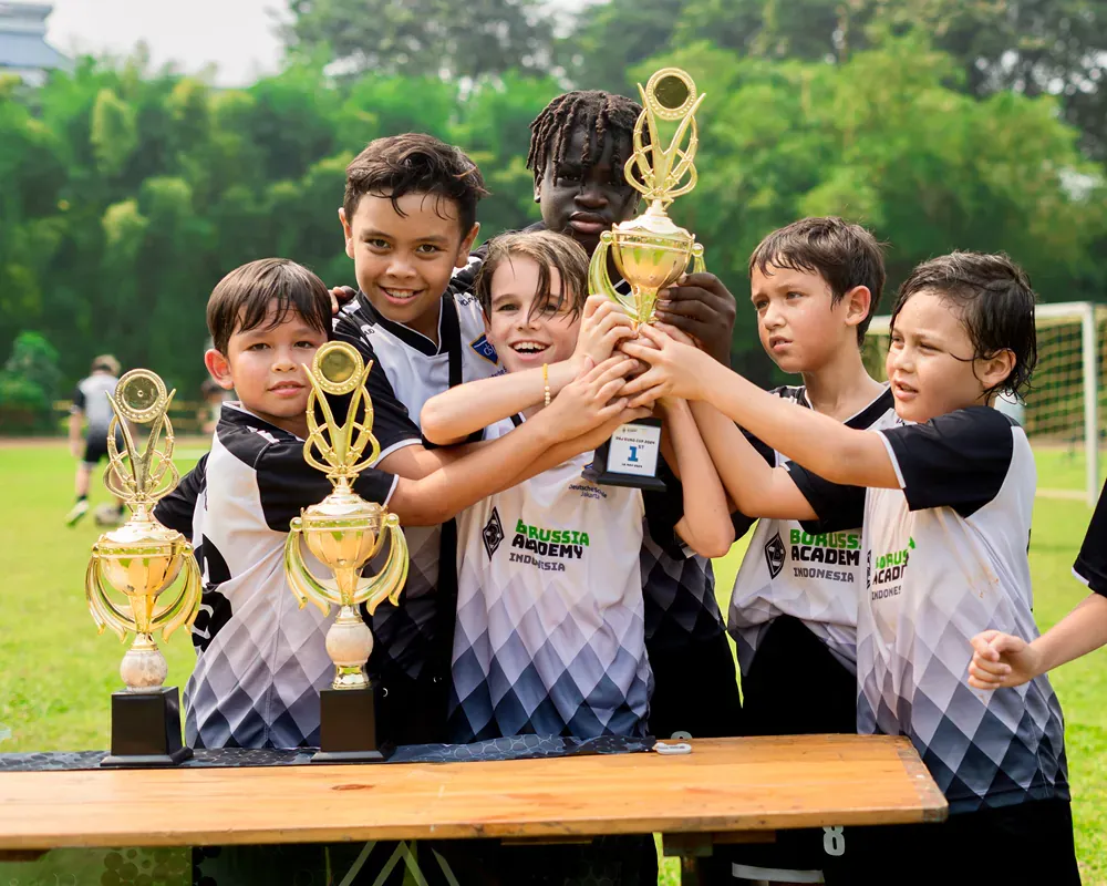 A group of young boys are putting their hands together in front of trophies.
