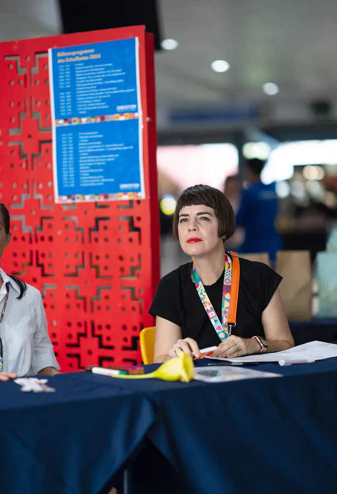 A woman is sitting at a table in front of a red wall.