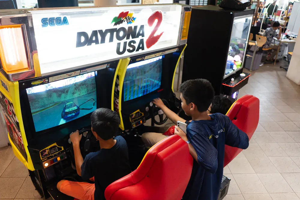 A group of people are playing a video game called daytona usa 2.