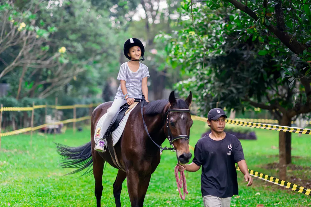 A little girl is riding a horse with a man walking behind her.