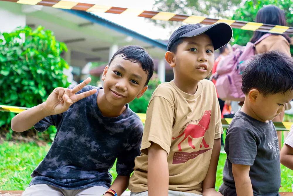 A group of young boys are sitting on a bench in the grass.