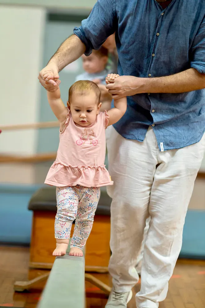 A man is helping a baby walk on a balance beam.