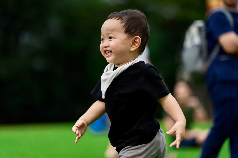 A little boy is running on the grass and smiling.