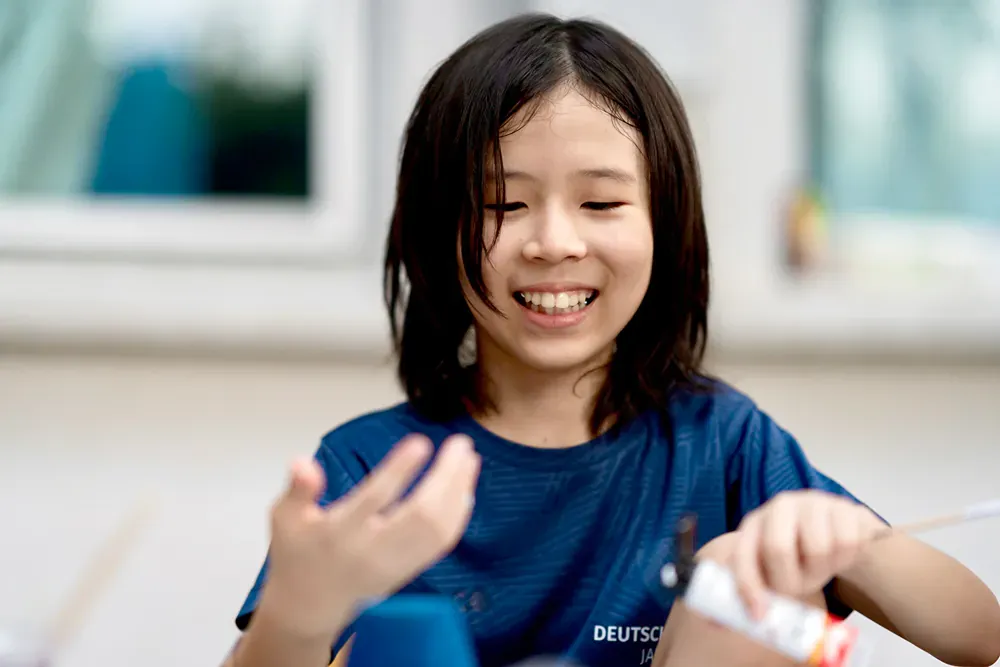 A young girl is smiling while holding a bottle of glue.
