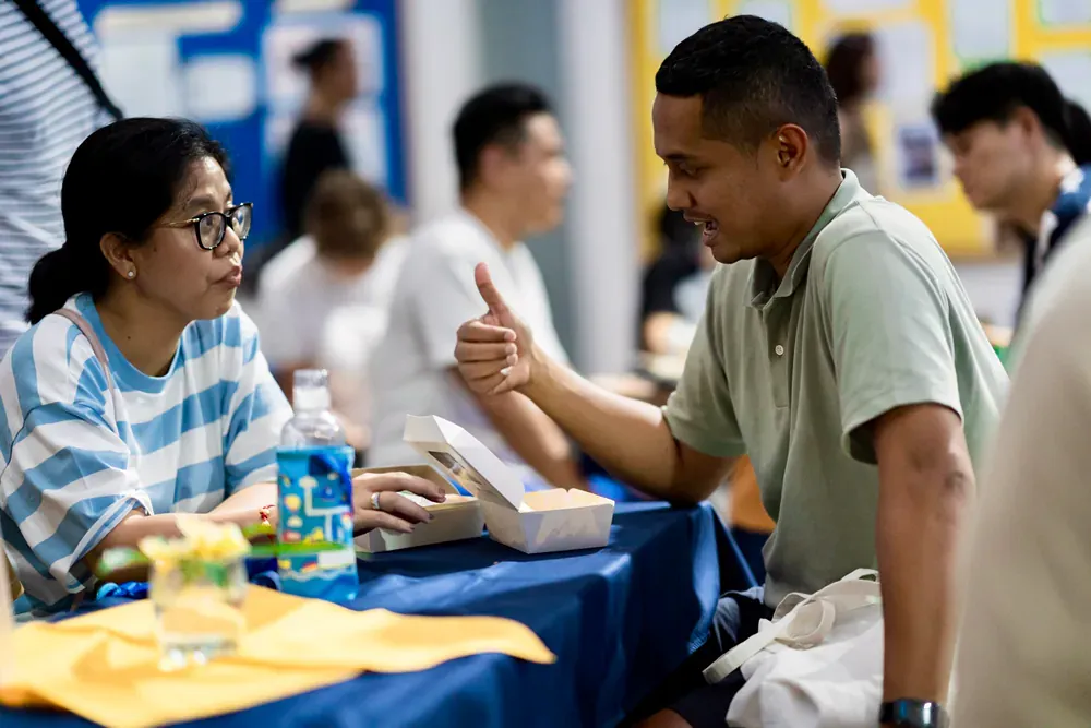 A man and a woman are sitting at a table talking to each other.
