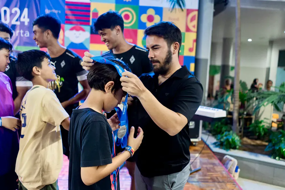 A man is putting a blue ribbon on a boy 's head while a group of children watch.