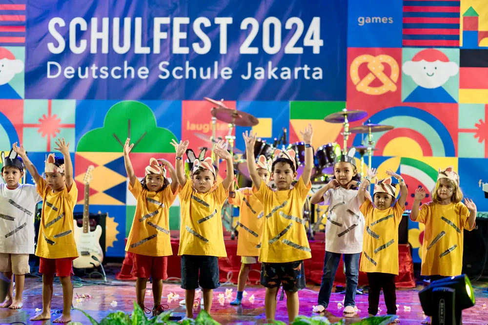 A group of children are standing on a stage in front of a sign that says schulfest 2024.