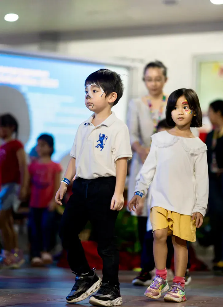 A boy and a girl are walking down a runway at a fashion show.