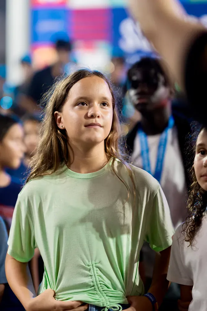 A young girl in a green shirt is standing in a crowd of people.