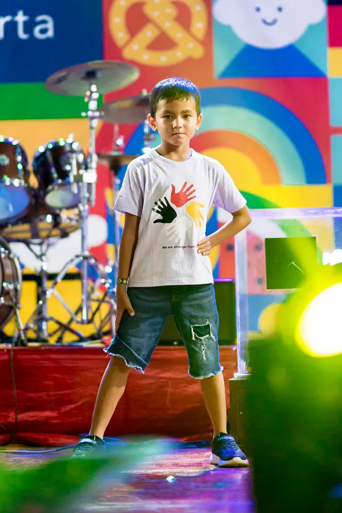 A young boy is standing on a stage in front of a drum set.