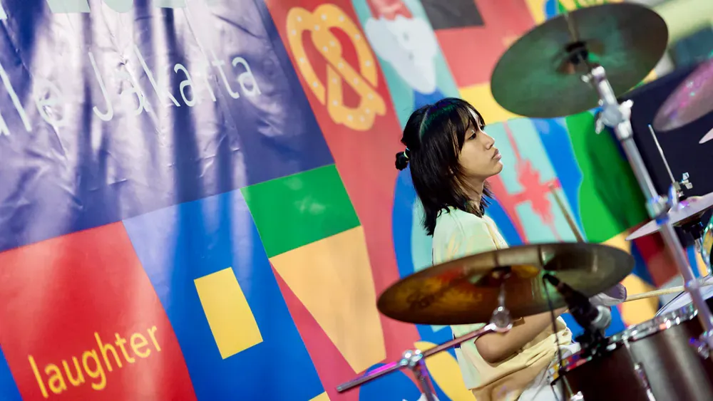 A woman is playing drums in front of a colorful wall.