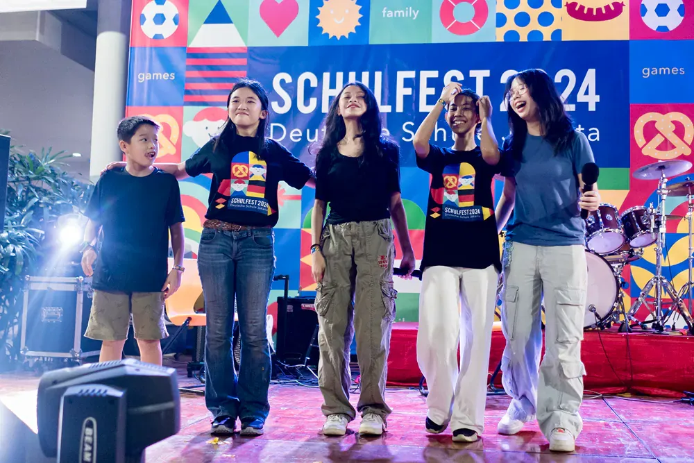A group of people are standing on a stage in front of a sign that says schulfest 24