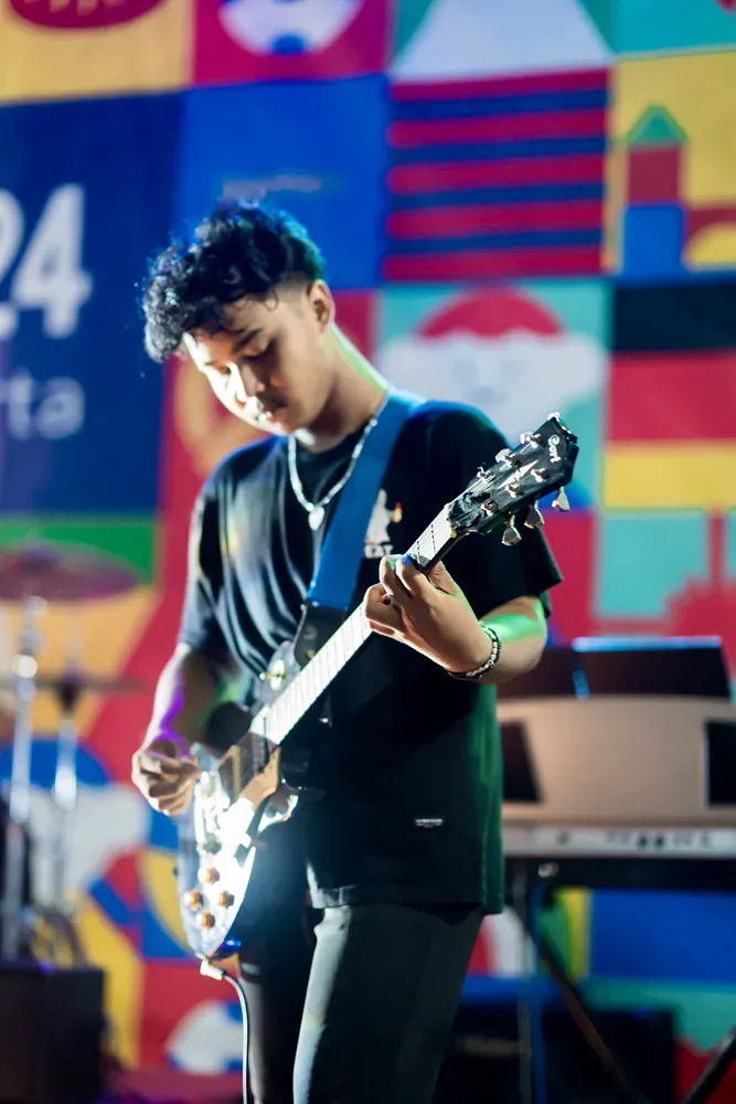 A young man is playing a guitar on stage in front of a colorful wall.