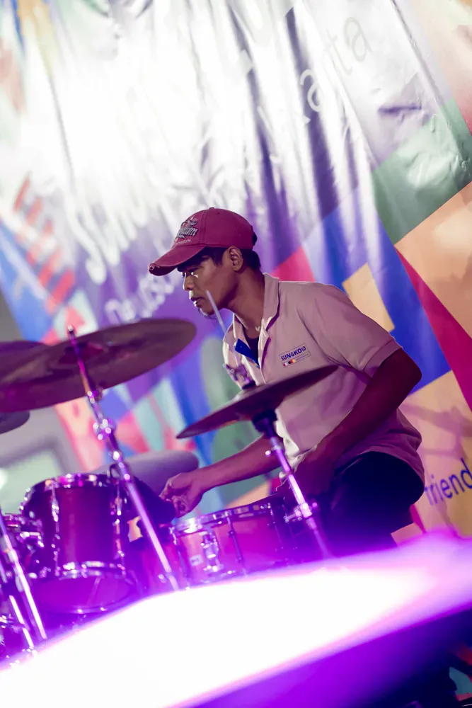 A man in a red hat is playing drums in front of a purple light
