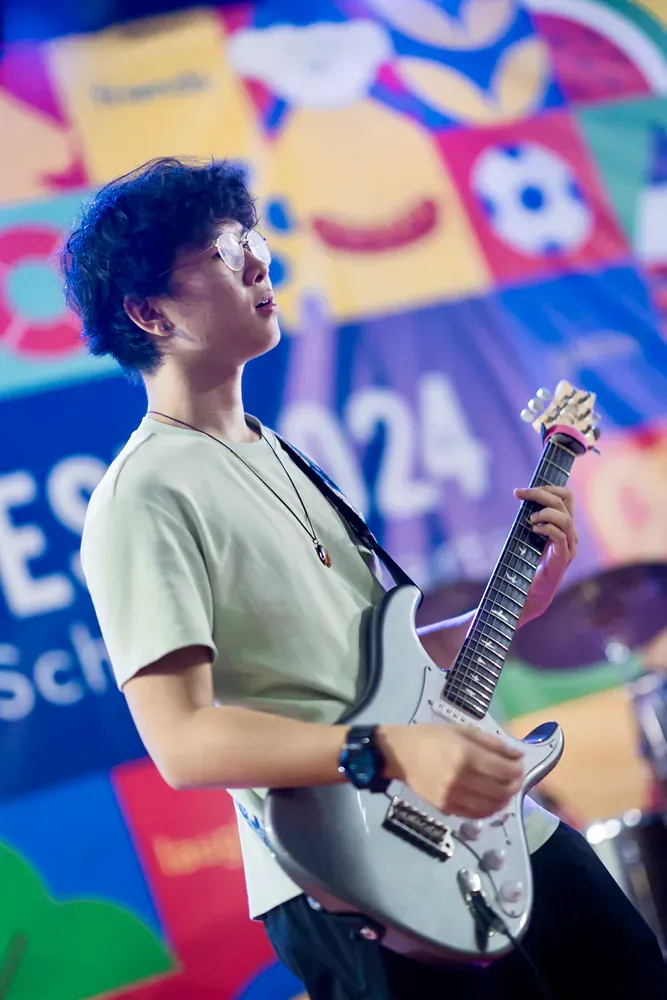 A young man is playing a guitar in front of a colorful background.