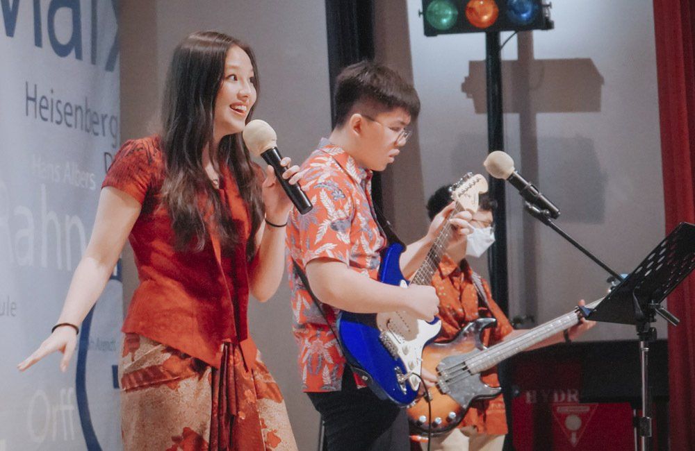 A woman is singing into a microphone while a man plays a guitar.