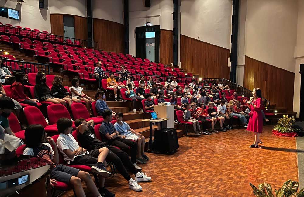 A woman is giving a speech in front of a large audience in an auditorium.