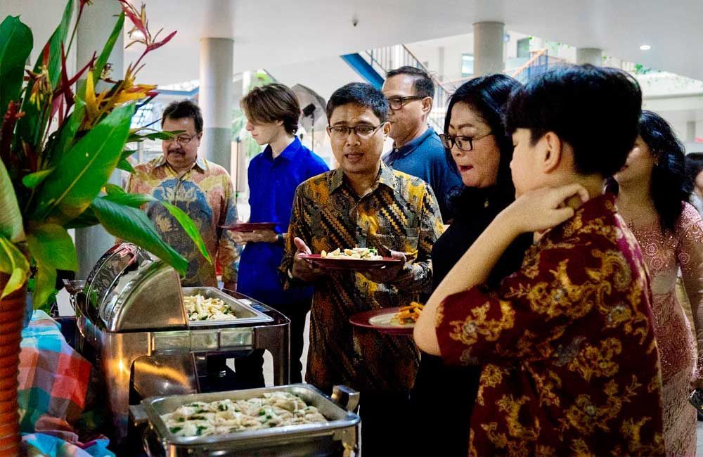 A group of people are standing around a buffet table eating food.