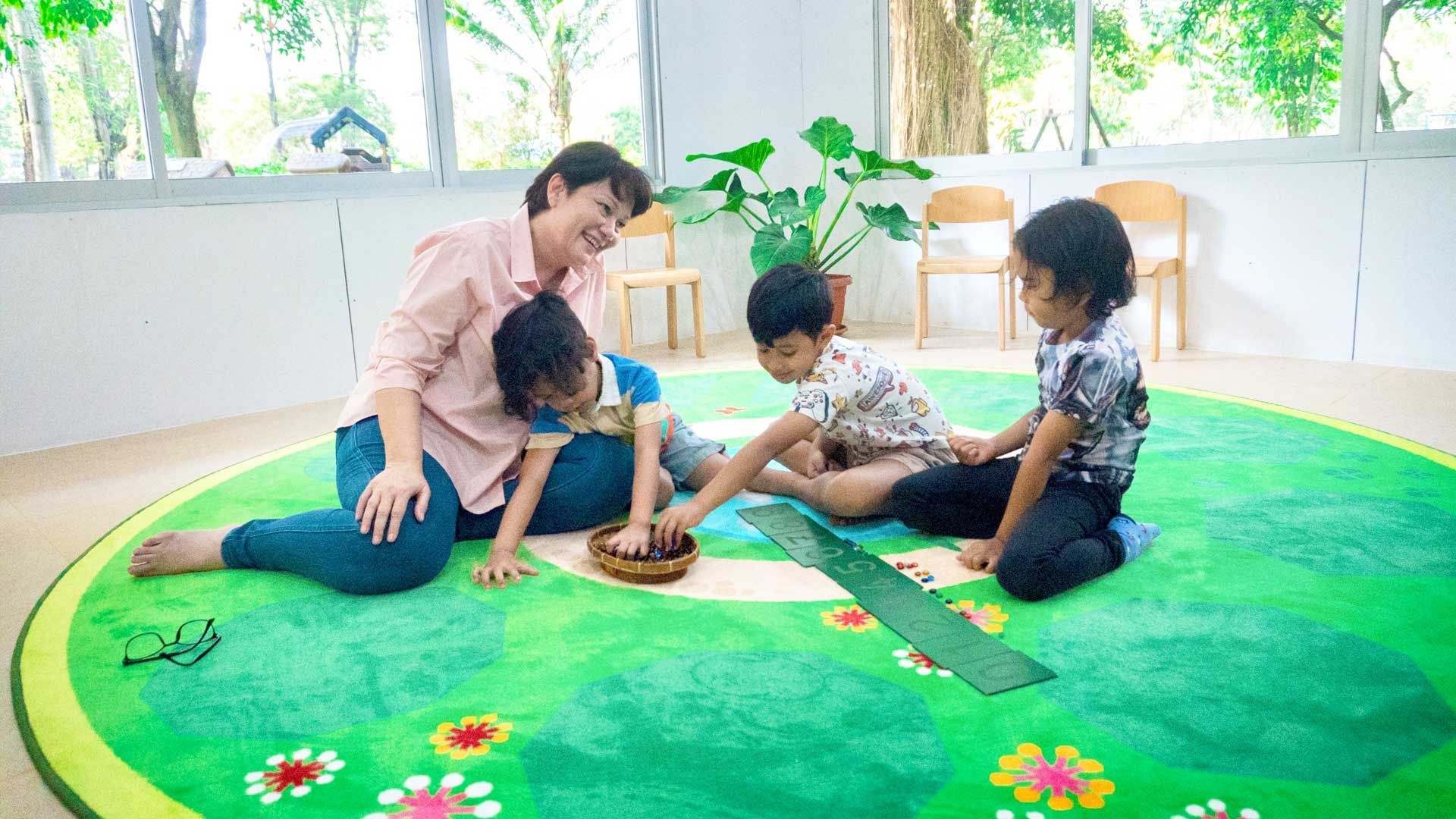 A woman and three children are sitting on a green rug.