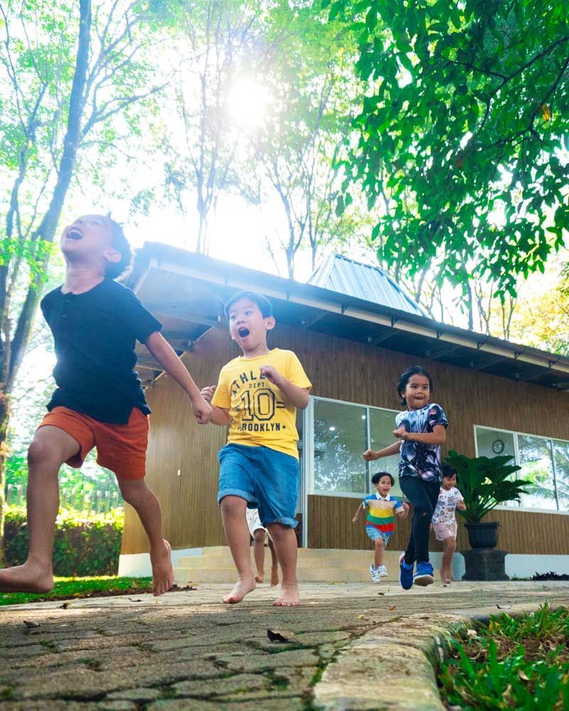 A group of children are holding hands and running in front of a building.