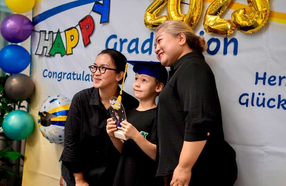 Three people are posing for a picture in front of a sign that says happy graduation.
