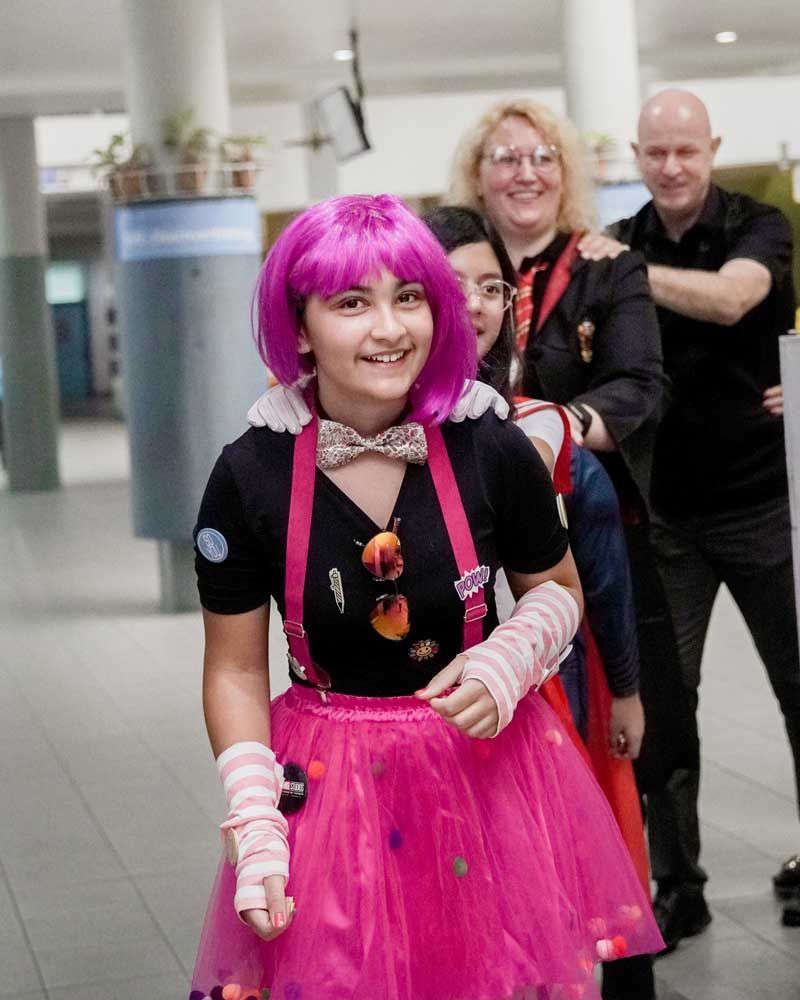 A girl with pink hair and a pink tutu is walking with a group of people