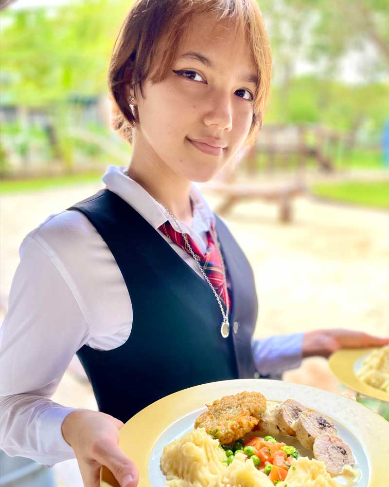 A young girl in a school uniform is holding a plate of food.
