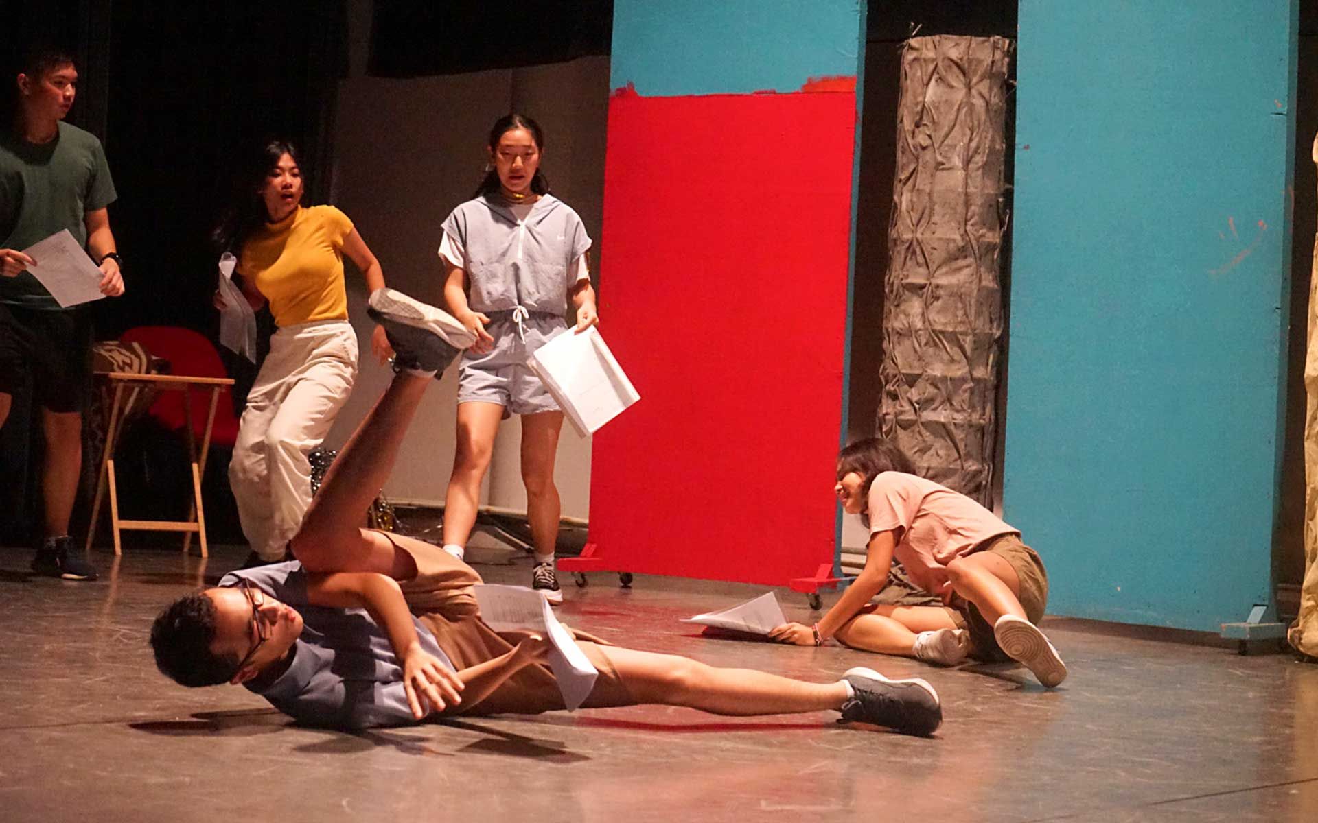 A group of people are standing around a man laying on the floor.