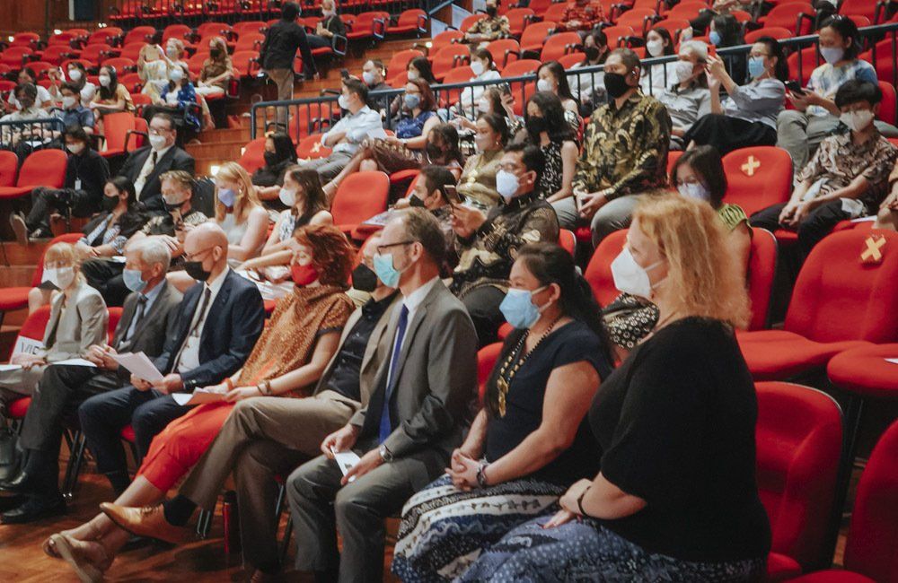 A large group of people wearing face masks are sitting in a theater.
