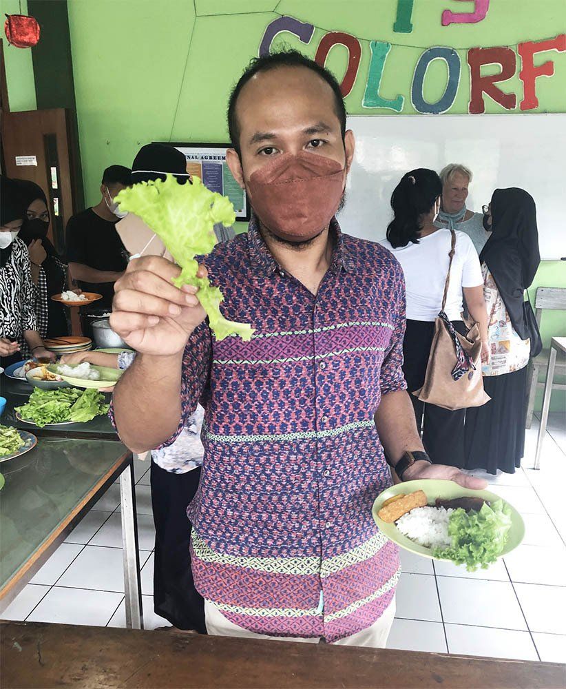 A man wearing a mask is holding a piece of lettuce and a plate of food.