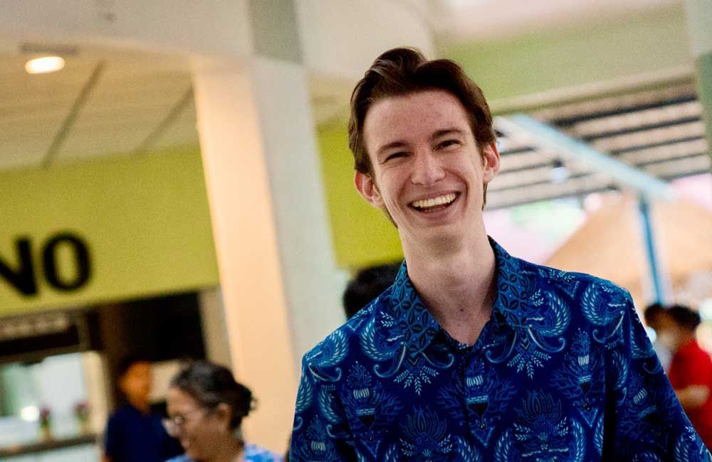 A man in a blue shirt is smiling in front of a no sign.