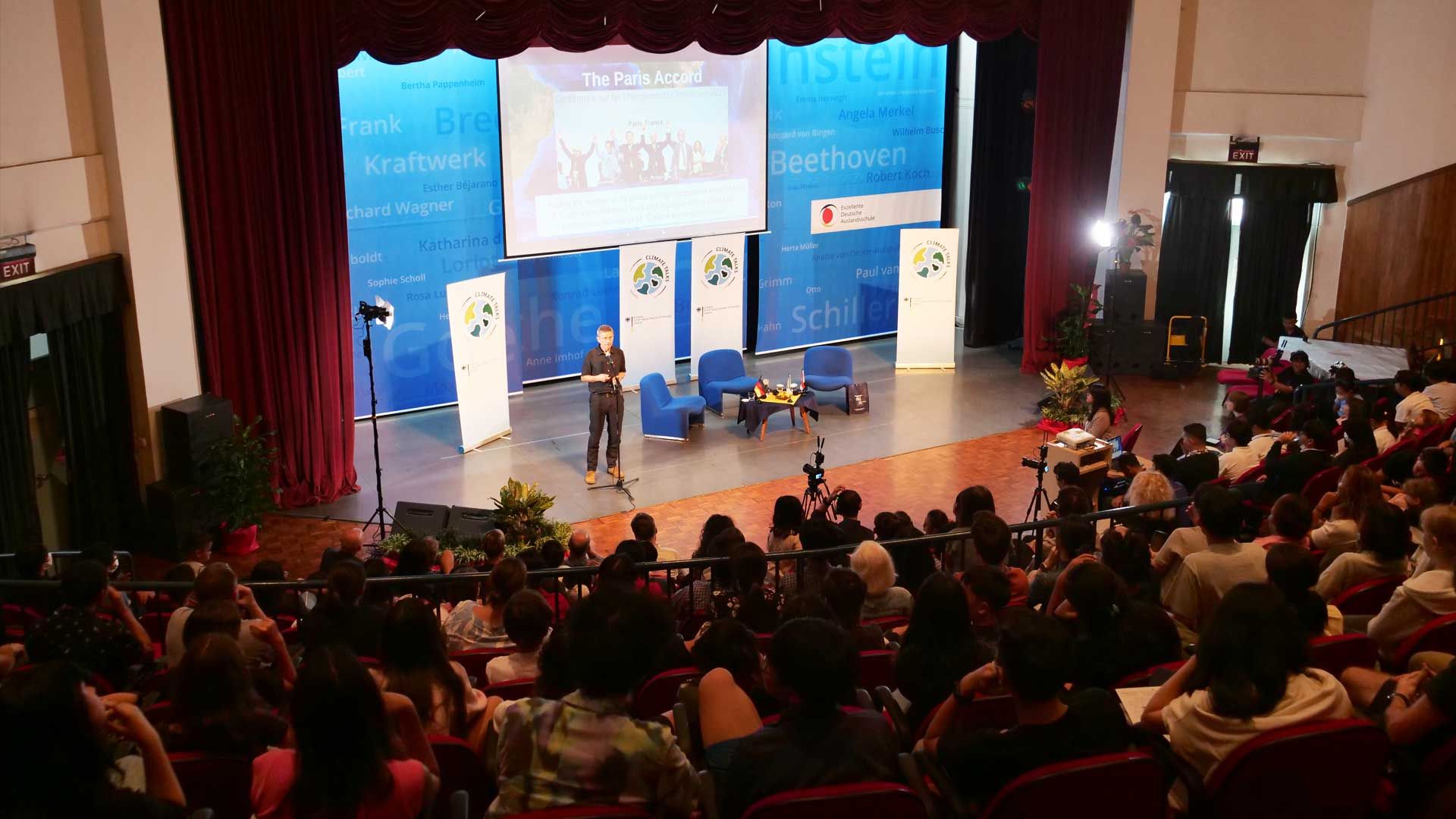 A woman is standing on a stage in front of a crowd of people.