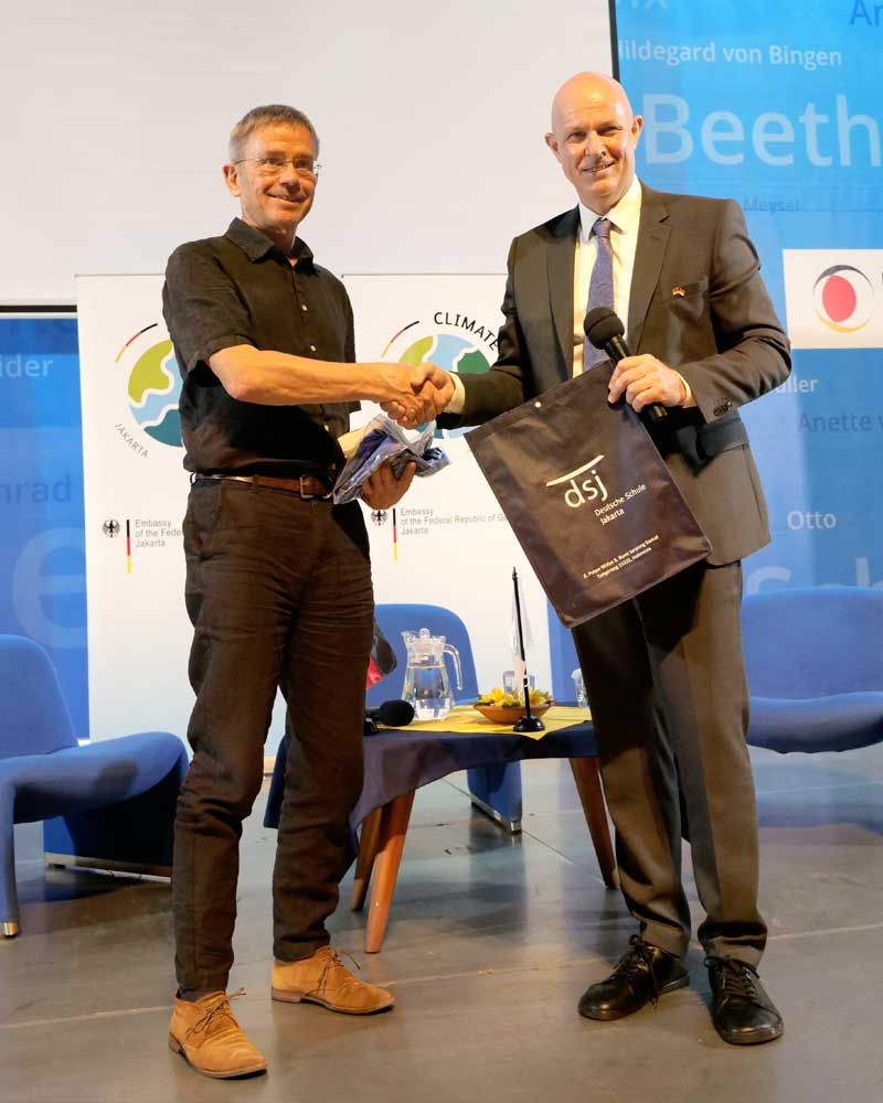 A man in a suit is shaking hands with another man in a black shirt.