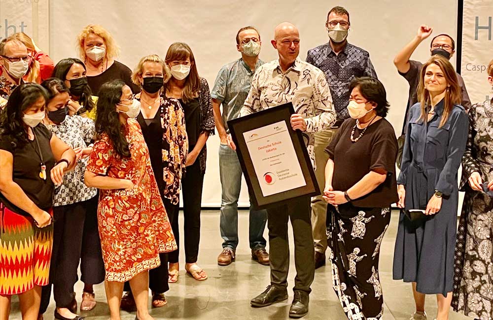 A group of people wearing face masks are standing around a man holding a certificate.