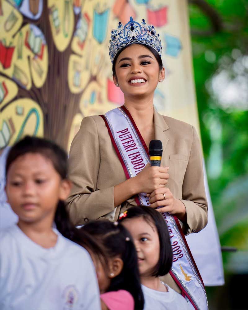 A woman wearing a crown is holding a microphone in front of a group of children