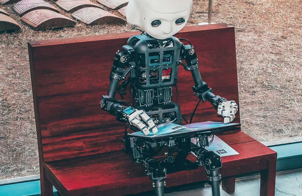 A robot is sitting on a wooden bench holding a skateboard.