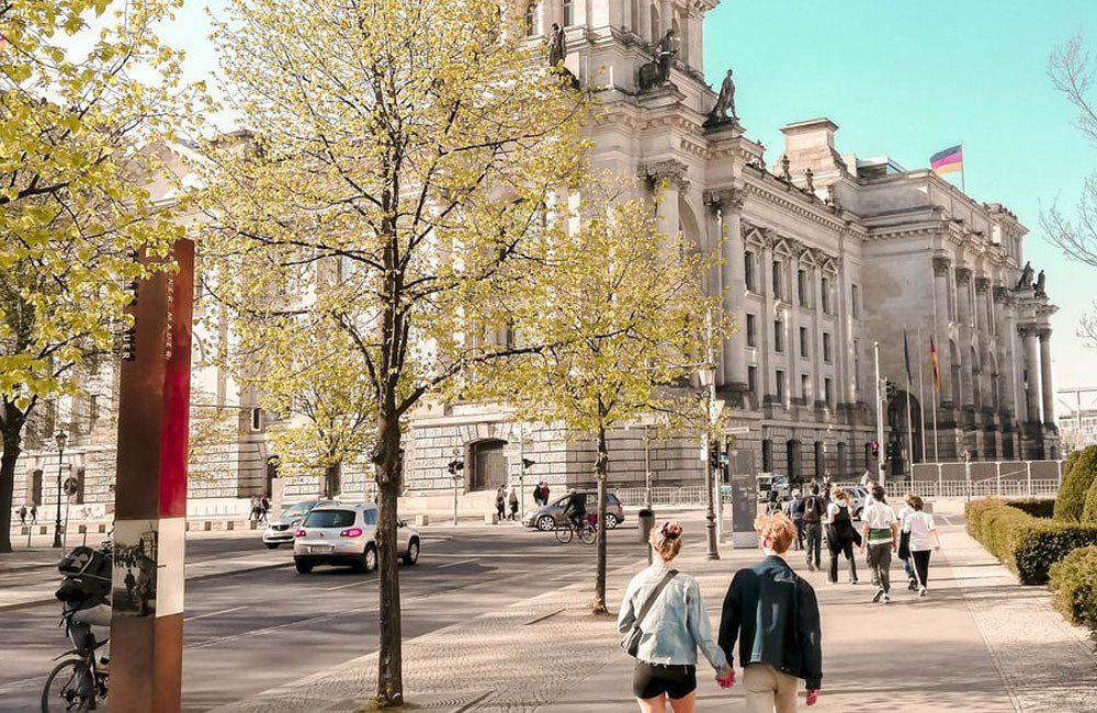 A couple of people are walking down a sidewalk in front of a large building.