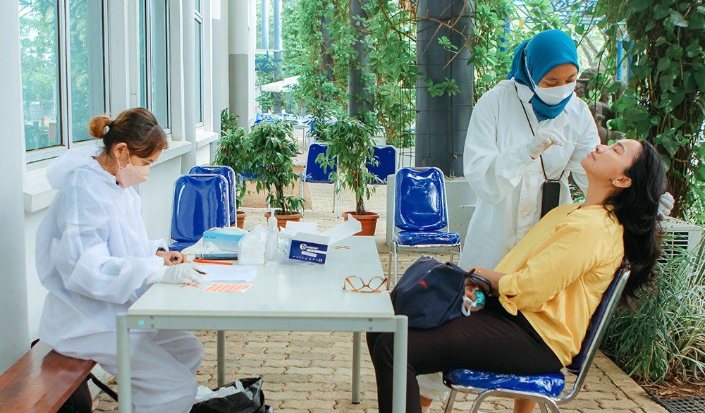 A woman is sitting at a table while a doctor takes a sample from her nose.