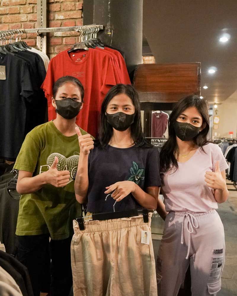 Three women wearing face masks are giving a thumbs up in a clothing store.