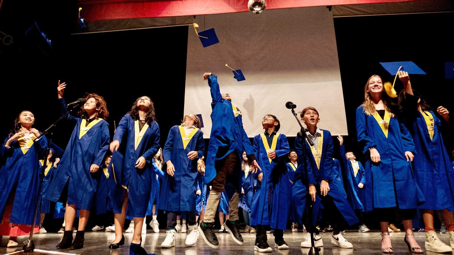 A group of children in graduation gowns are throwing their caps in the air.