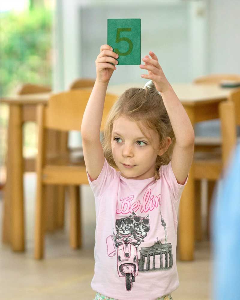 A little girl is holding up a card with the number 5 on it.