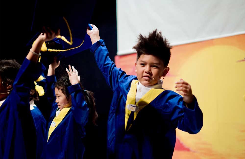 A group of children in graduation gowns are dancing on a stage.