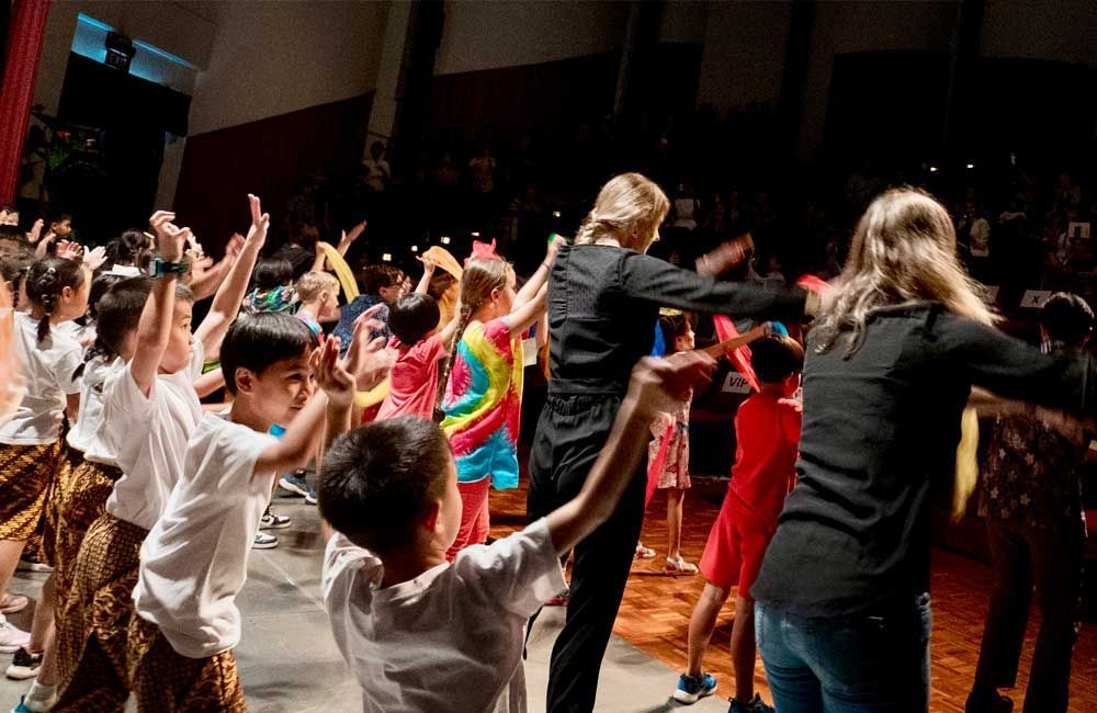 A group of children are dancing on a stage with their hands in the air.