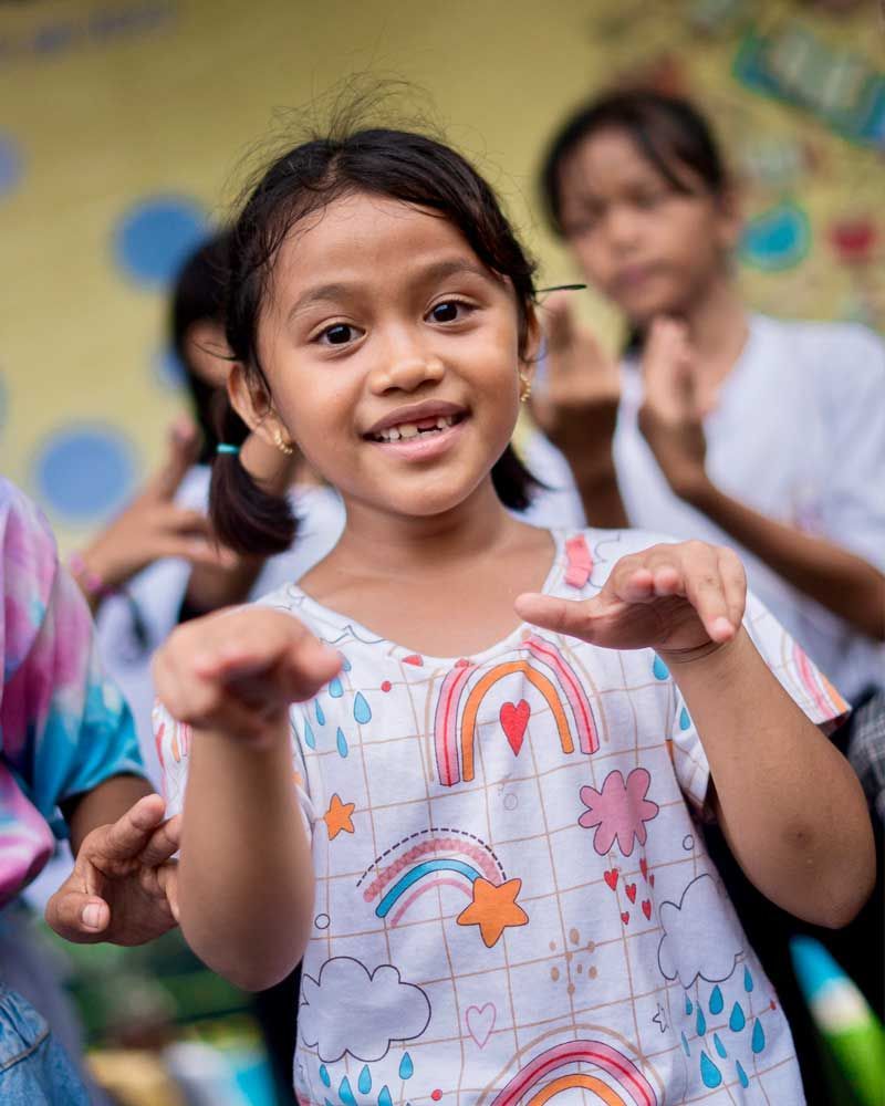 A little girl in a rainbow shirt is dancing with other children.
