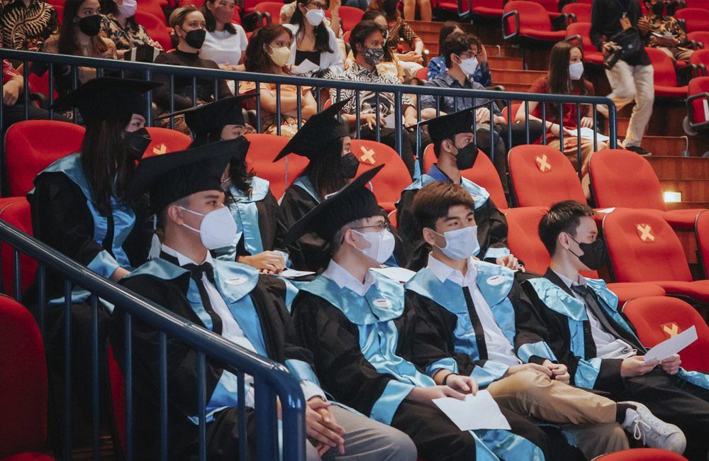 A group of graduates wearing masks are sitting in an auditorium.