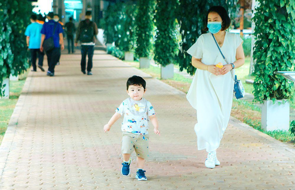A woman wearing a mask is walking with a child on a sidewalk.